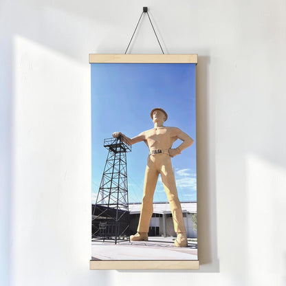 Golden Driller Tulsa canvas wall art hanging on a white wall, showing the Oklahoma landmark and oil derrick in a vertical 12 x 24 inch photograph with wood rails