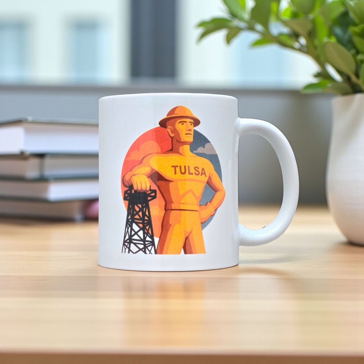 Tulsa Golden Driller coffee mug on wood desk with books and plant, 11oz ceramic mug featuring Tulsa landmark artwork