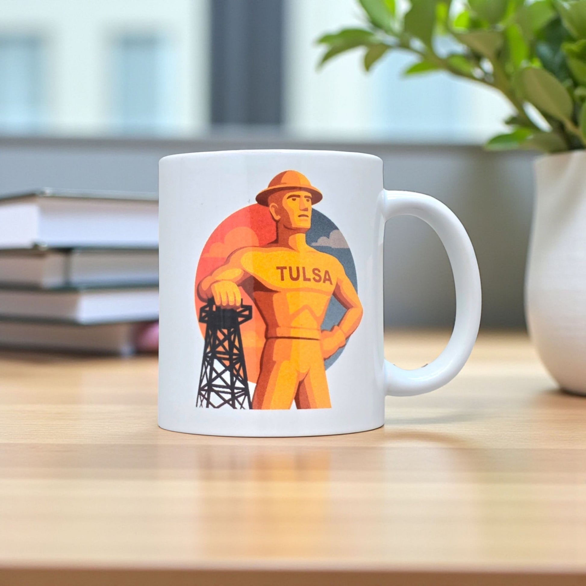 Tulsa Golden Driller coffee mug on wood desk with books and plant, 11oz ceramic mug featuring Tulsa landmark artwork