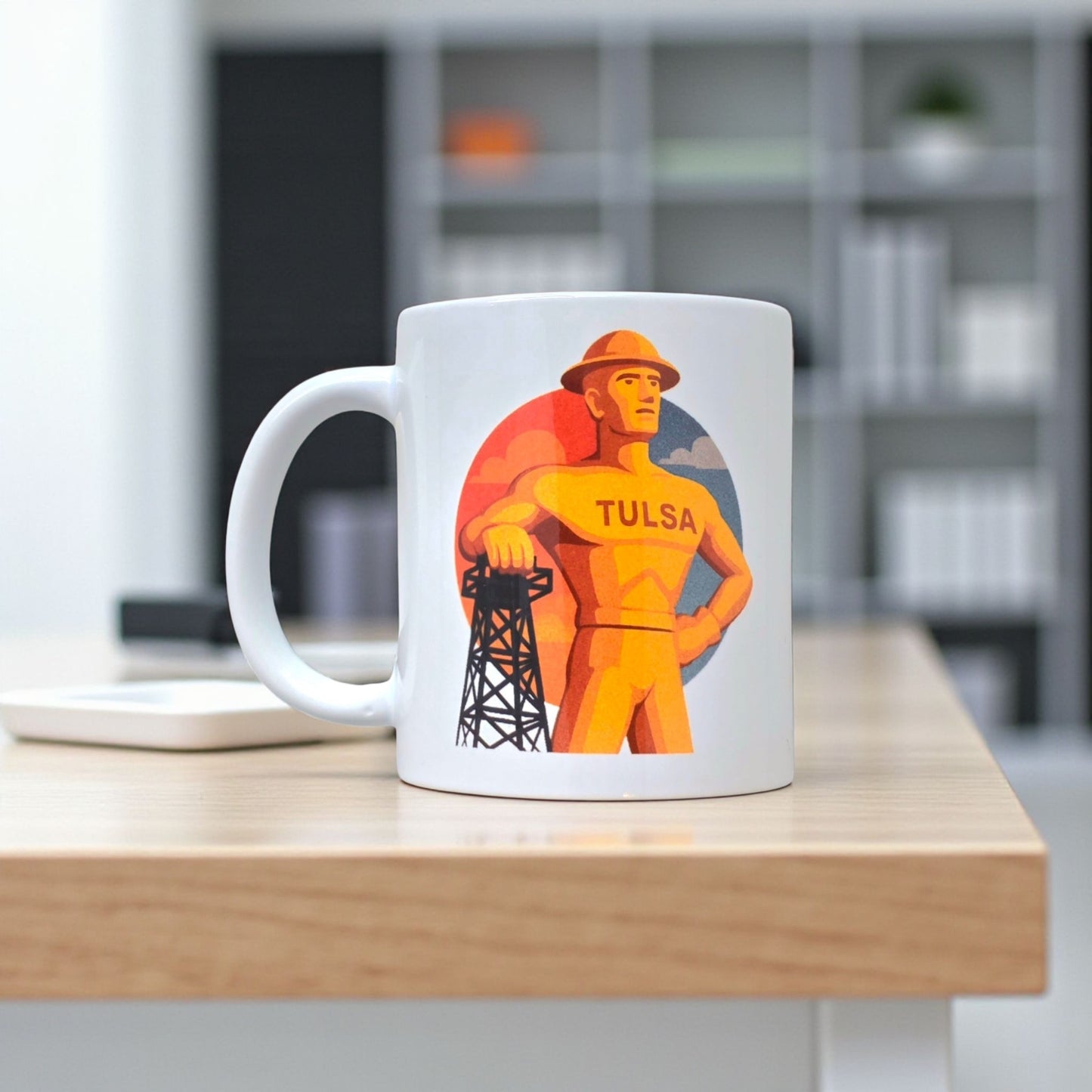 Tulsa Golden Driller coffee mug displayed on office table, white ceramic mug with bold Tulsa illustration for local pride or travel gift