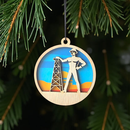 Tulsa Golden Driller wooden ornament hanging on evergreen tree, layered wood Tulsa landmark ornament used as Oklahoma Christmas decor or Route 66 souvenir
