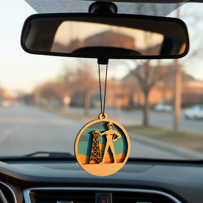 Layered wooden Tulsa Golden Driller sunset car ornament hanging from rearview mirror, round design with oil derrick and driller silhouette against colorful sunset background, lightweight auto accessory gift for Tulsa locals, Oklahoma travelers, and Route 66 souvenir collectors