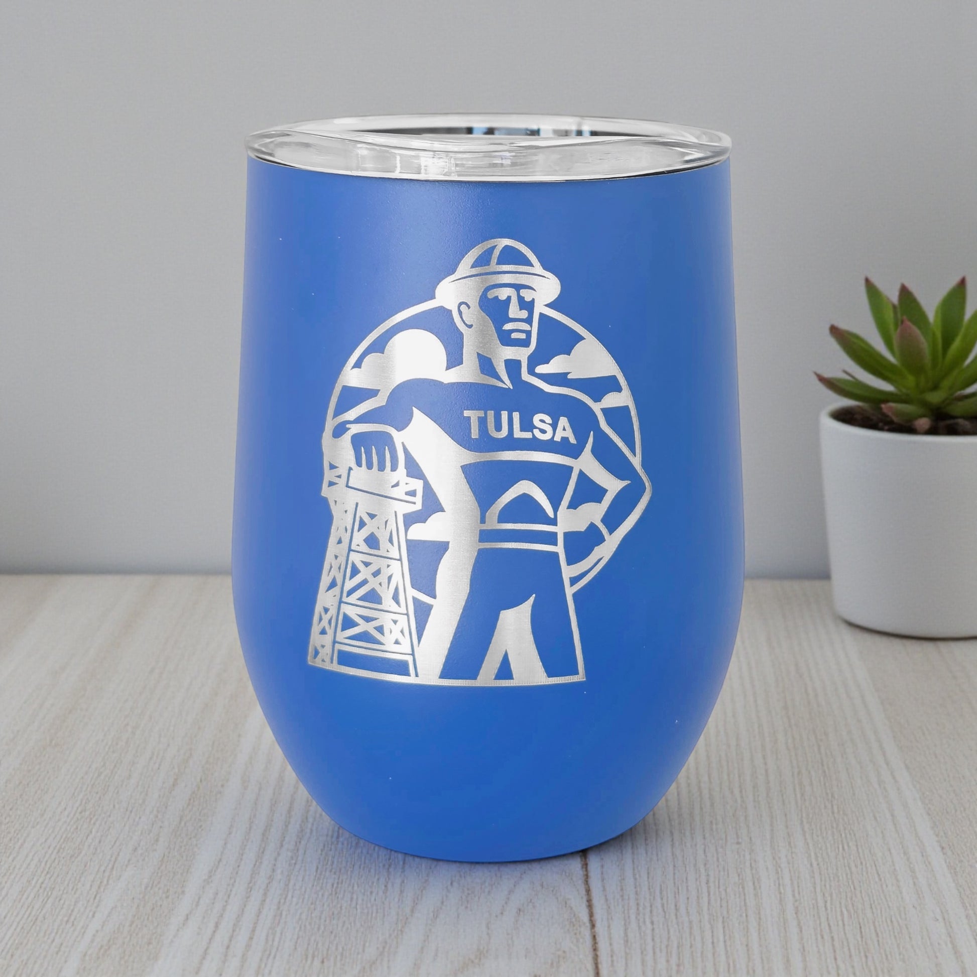 Blue Tulsa Golden Driller 12oz wine tumbler standing on table, engraved Oklahoma drinkware used as Tulsa gift or travel souvenir