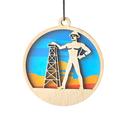 Tulsa Golden Driller wooden ornament with layered wood figure and oil rig over a sunset background, round Tulsa ornament with hanging cord for local gift or souvenir