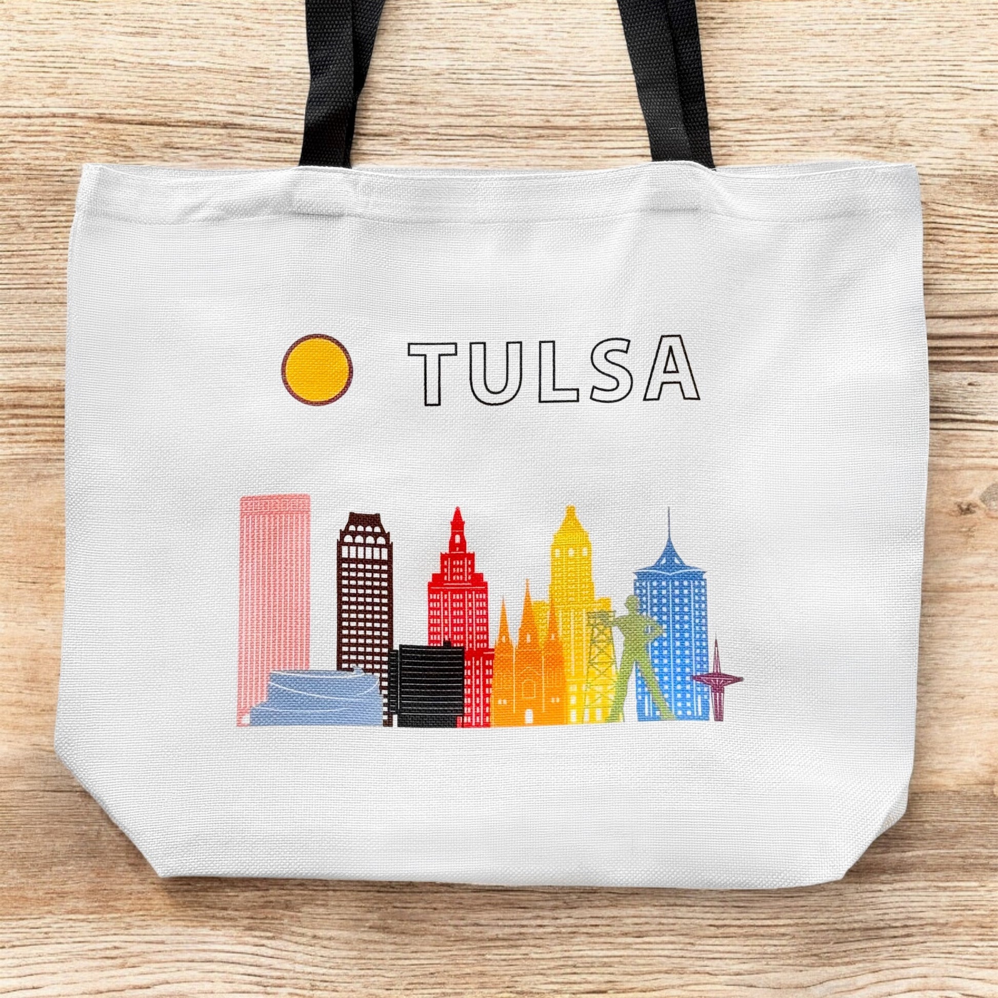 Large Tulsa LGBTQIA pride skyline tote bag shown flat on wood surface with colorful Tulsa landmark illustration