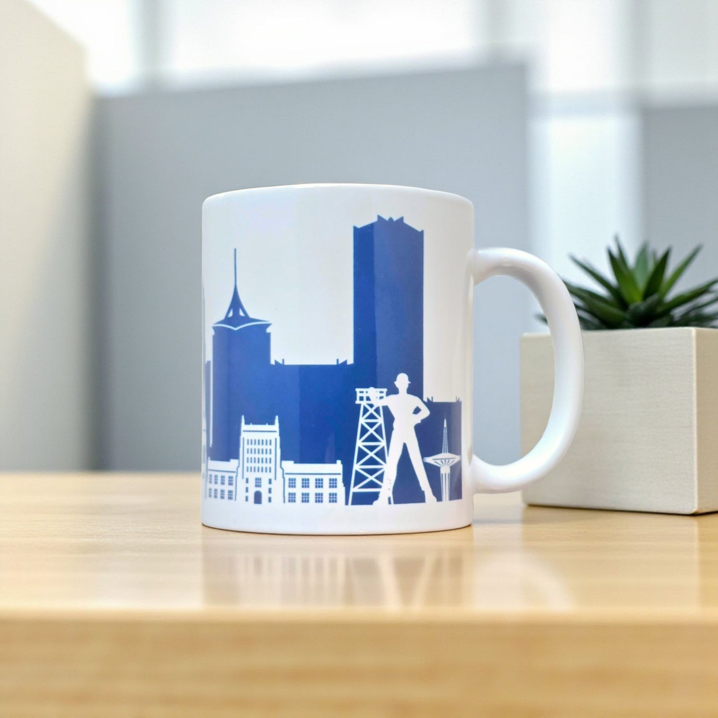 Tulsa navy skyline coffee mug displayed on wood table with plant, 11oz ceramic mug featuring downtown Tulsa skyline artwork