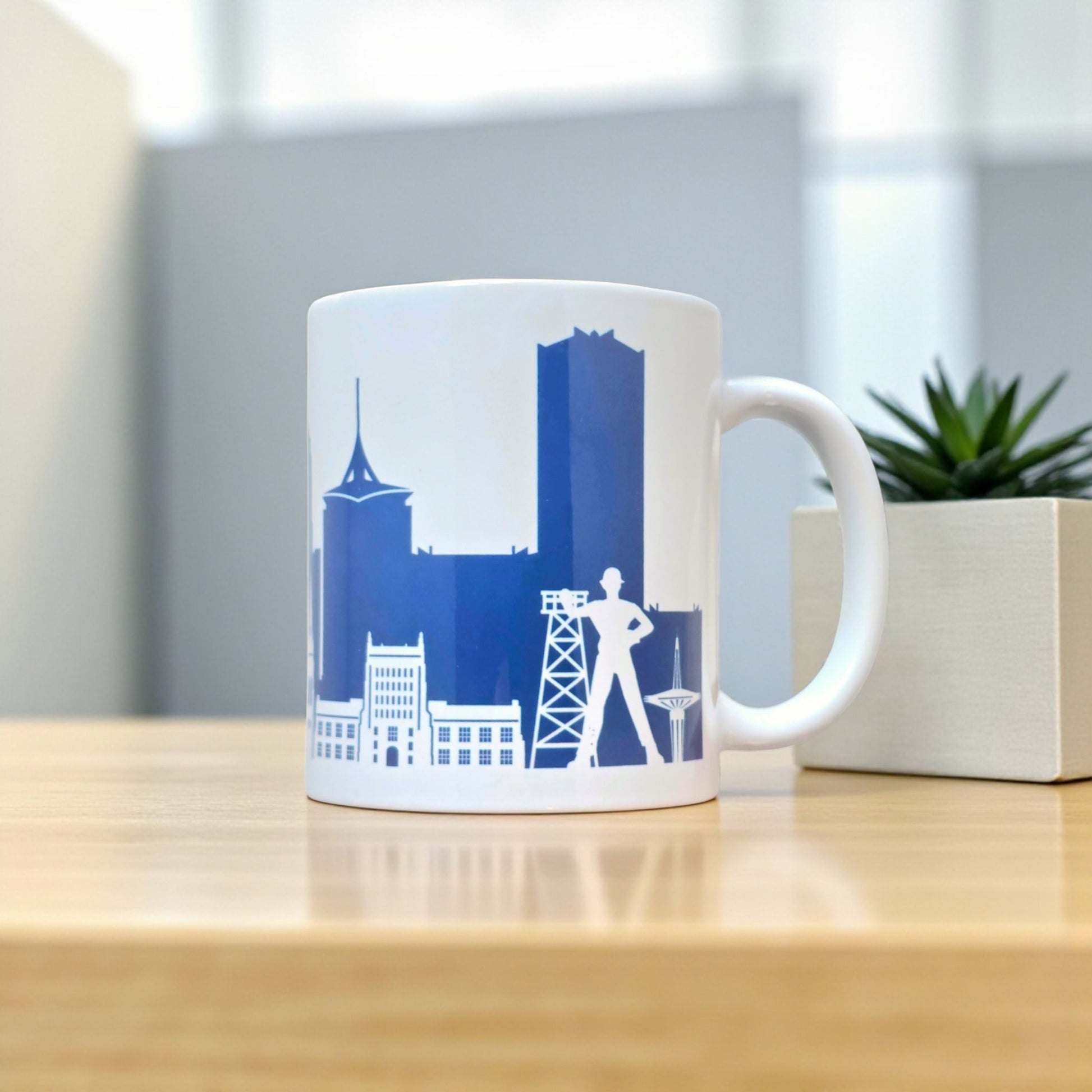 Tulsa navy skyline coffee mug displayed on wood table with plant, 11oz ceramic mug featuring downtown Tulsa skyline artwork