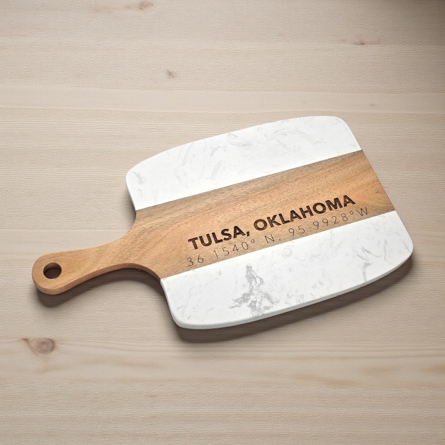Angled view of Tulsa Oklahoma charcuterie board with engraved coordinates, white marble and acacia wood serving board for entertaining, wedding gifts, or Tulsa home decor