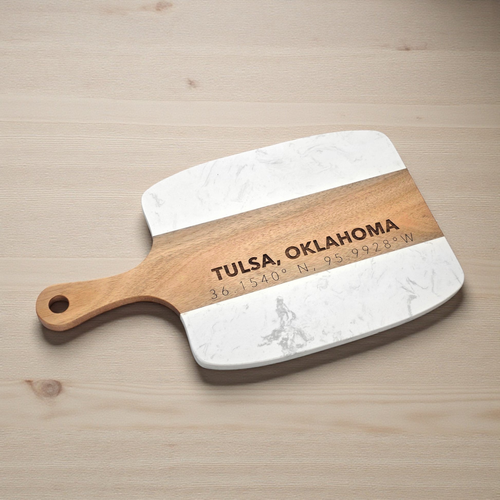 Angled view of Tulsa Oklahoma charcuterie board with engraved coordinates, white marble and acacia wood serving board for entertaining, wedding gifts, or Tulsa home decor