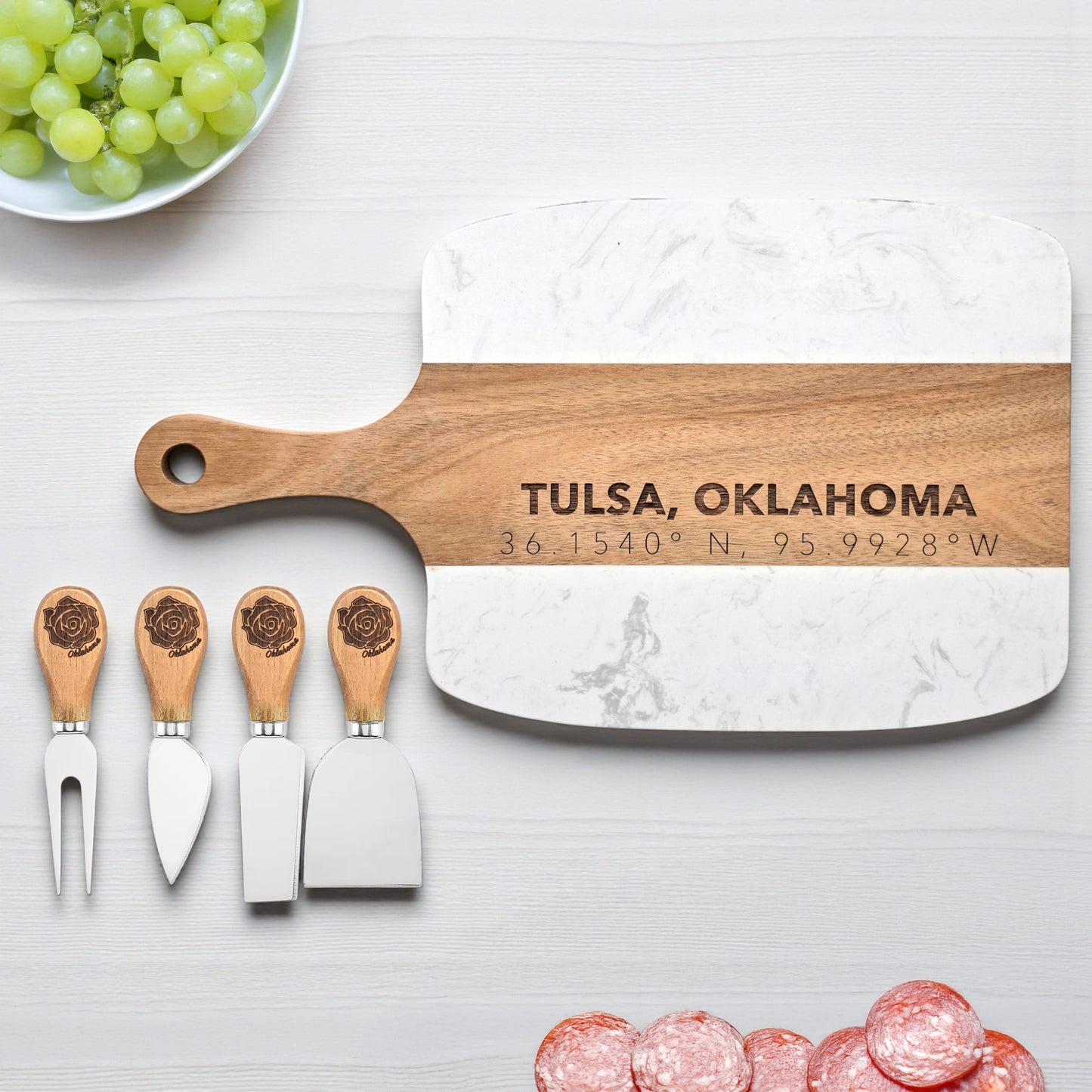 Tulsa Oklahoma marble and wood serving board engraved with coordinates beside matching cheese knives, styled with grapes and meats, useful Tulsa kitchen gift and Oklahoma souvenir