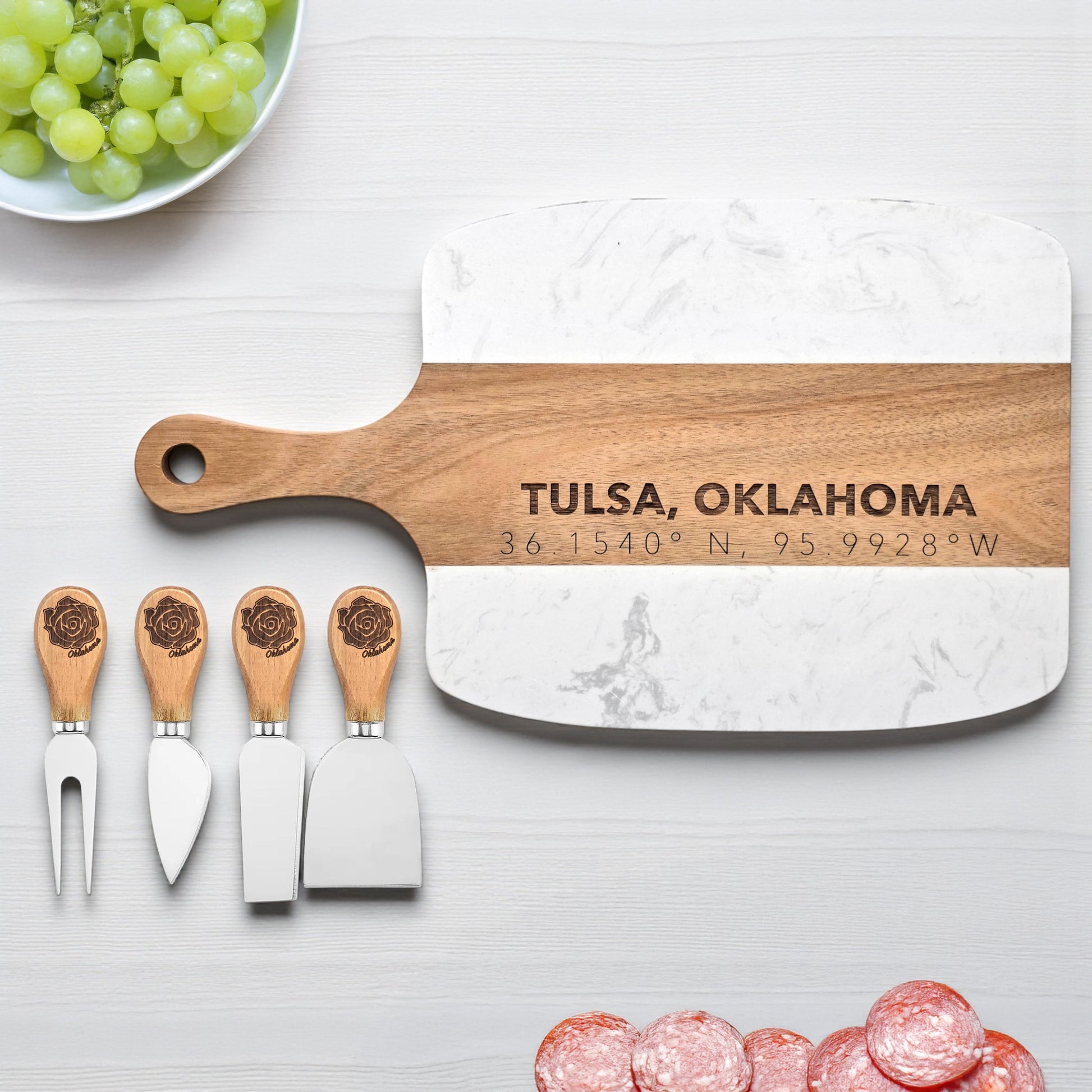 Tulsa Oklahoma marble and wood serving board engraved with coordinates beside matching cheese knives, styled with grapes and meats, useful Tulsa kitchen gift and Oklahoma souvenir