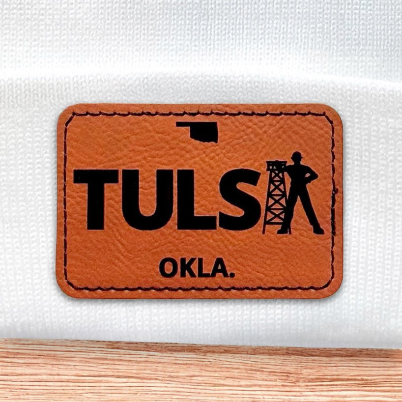 Close up of Tulsa Oklahoma leatherette patch showing TULSA text and oil derrick design on white knit beanie