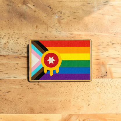 Tulsa Pride lapel pin made from Eco Wood Birch featuring rainbow Tulsa flag inspired design displayed on wood table