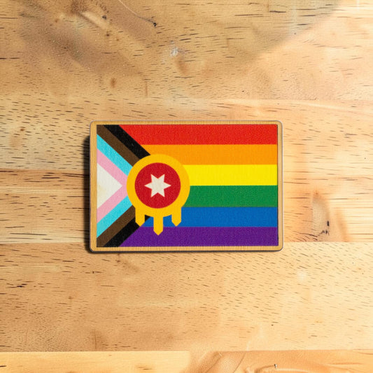 Tulsa Pride lapel pin made from Eco Wood Birch featuring rainbow Tulsa flag inspired design displayed on wood table