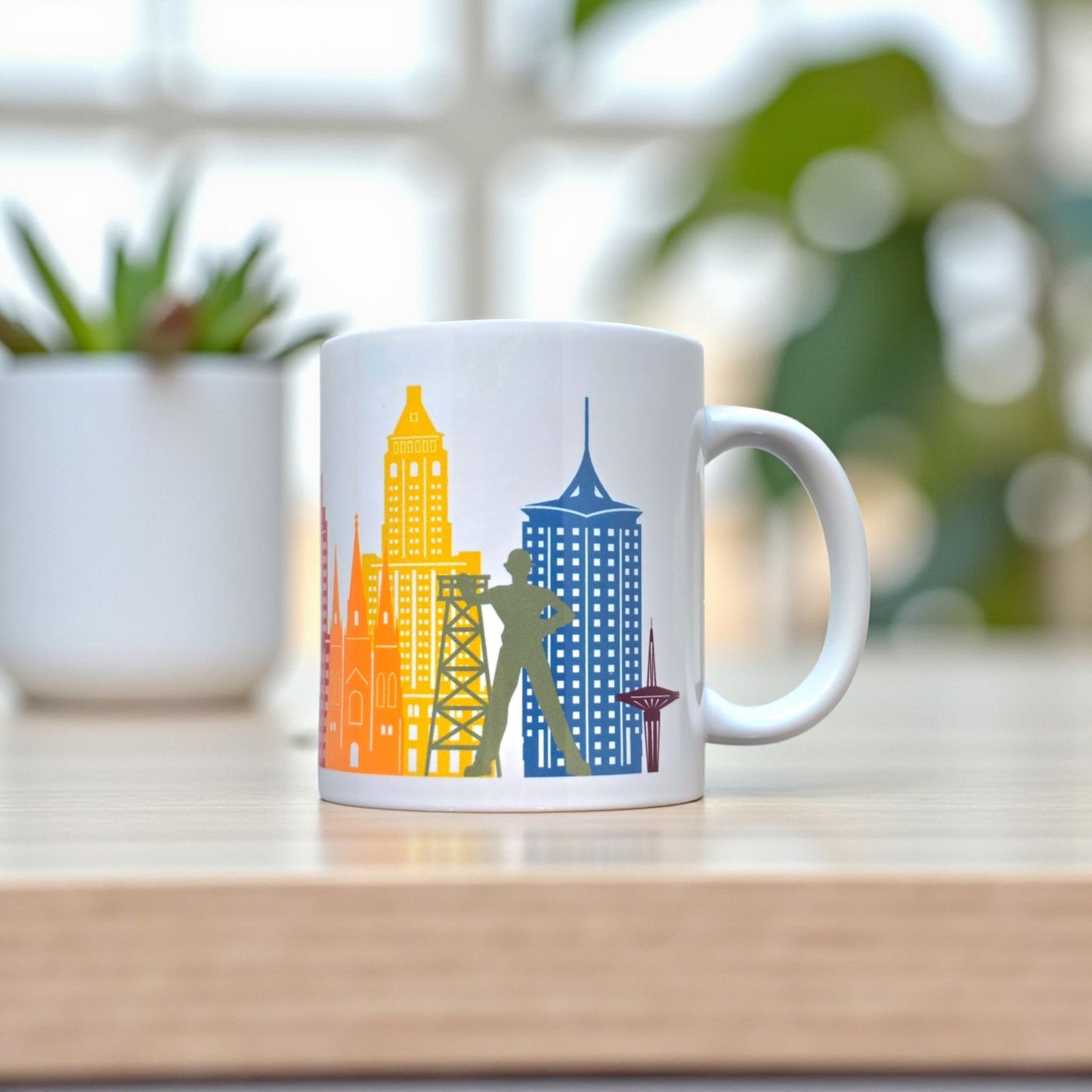 Tulsa rainbow skyline coffee mug displayed on wood table with plant, 11oz ceramic mug featuring colorful Tulsa skyline artwork