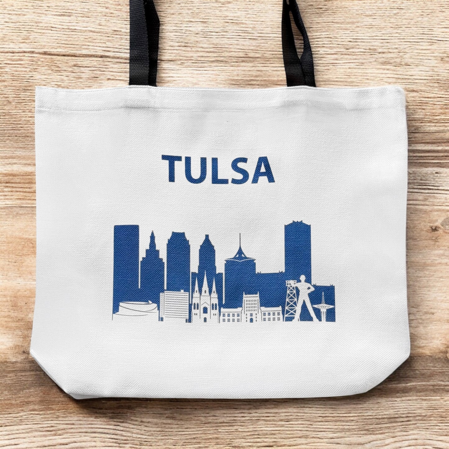 Large Tulsa skyline tote bag shown flat on wood surface featuring navy Tulsa city skyline design
