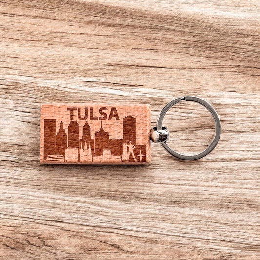 Laser engraved Tulsa skyline wooden keychain resting on wood surface, Tulsa city skyline keychain used as Oklahoma travel souvenir or everyday carry accessory