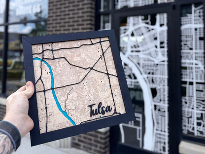 Hand holding framed Tulsa wooden city map, showing scale, engraved street detail, layered black roads, and painted river for Tulsa souvenir gift