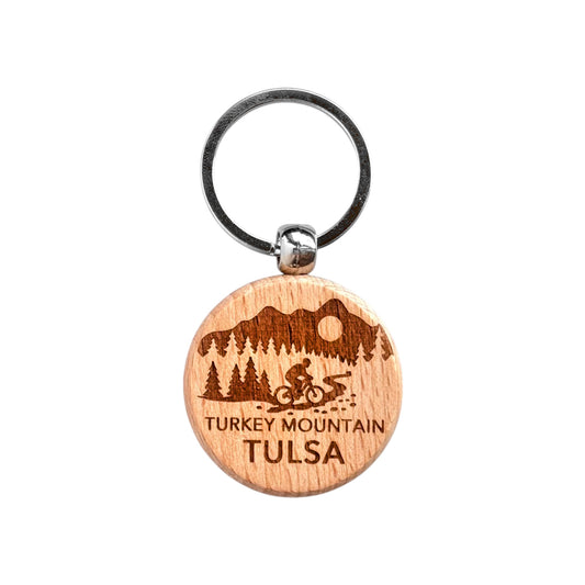 Round Turkey Mountain Tulsa wooden keychain with laser engraved cyclist on trail, trees, hills, and sun, lightweight wood keychain with metal ring for Tulsa souvenir or outdoor gift made in the USA