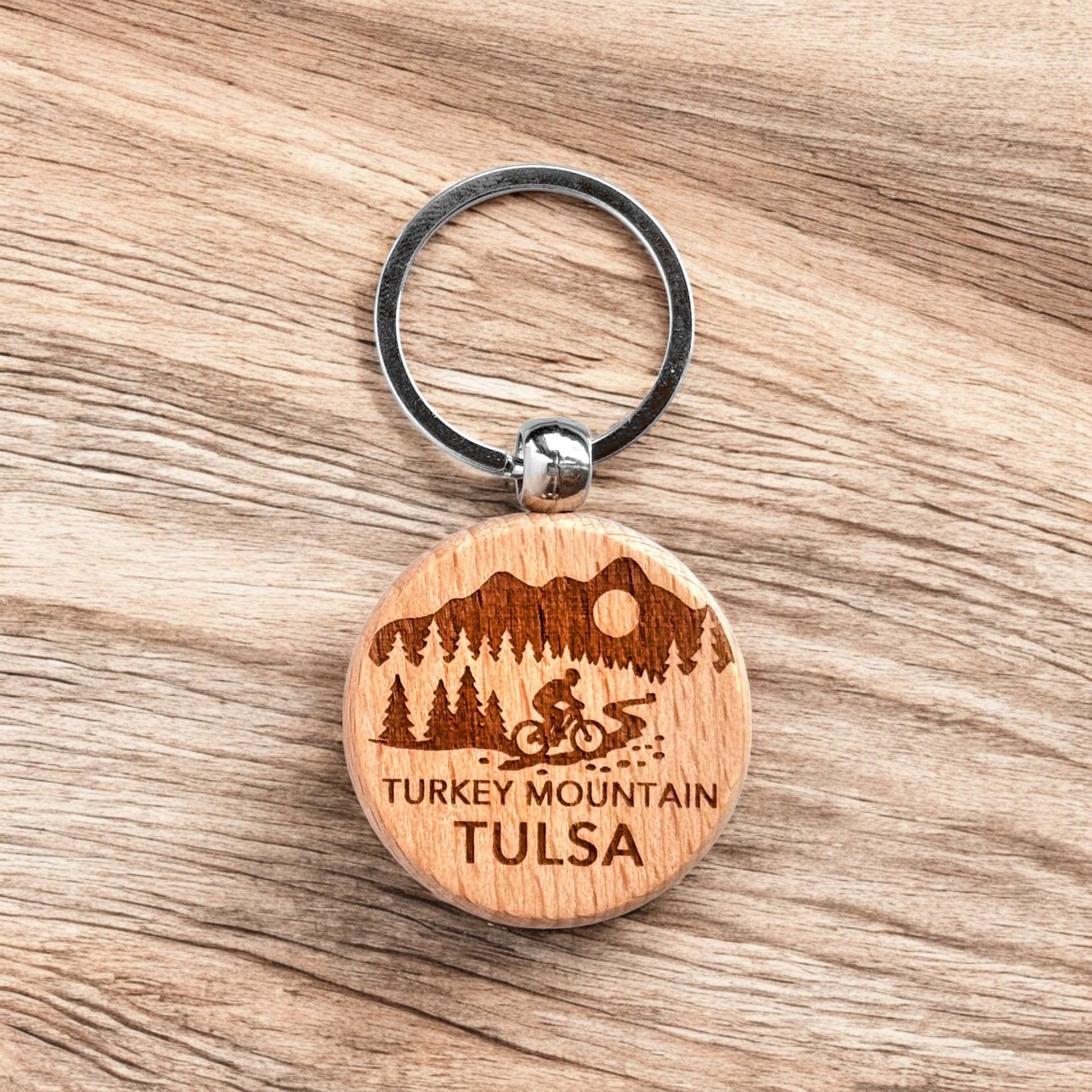 Laser engraved Turkey Mountain Tulsa wooden keychain resting on wood surface, local Tulsa trail keychain used as hiking gift, biking souvenir, or everyday carry accessory