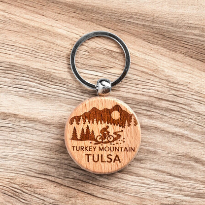 Laser engraved Turkey Mountain Tulsa wooden keychain resting on wood surface, local Tulsa trail keychain used as hiking gift, biking souvenir, or everyday carry accessory