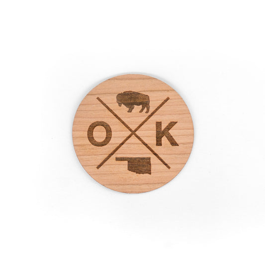 A circular wooden sticker featuring the OK-X design with a bison, Oklahoma state outline, and crossed lines, crafted with a 3M adhesive backing.